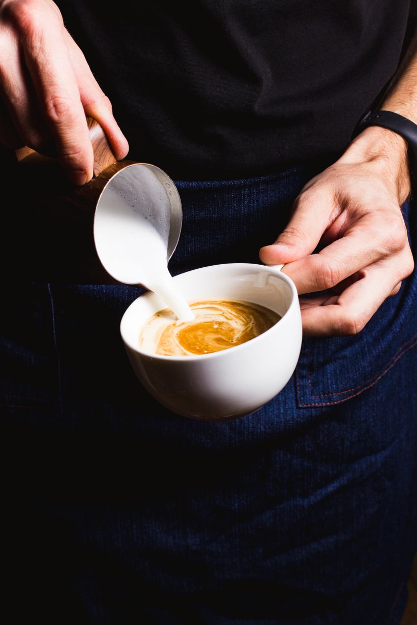 A barista pouring steamed milk into a coffee